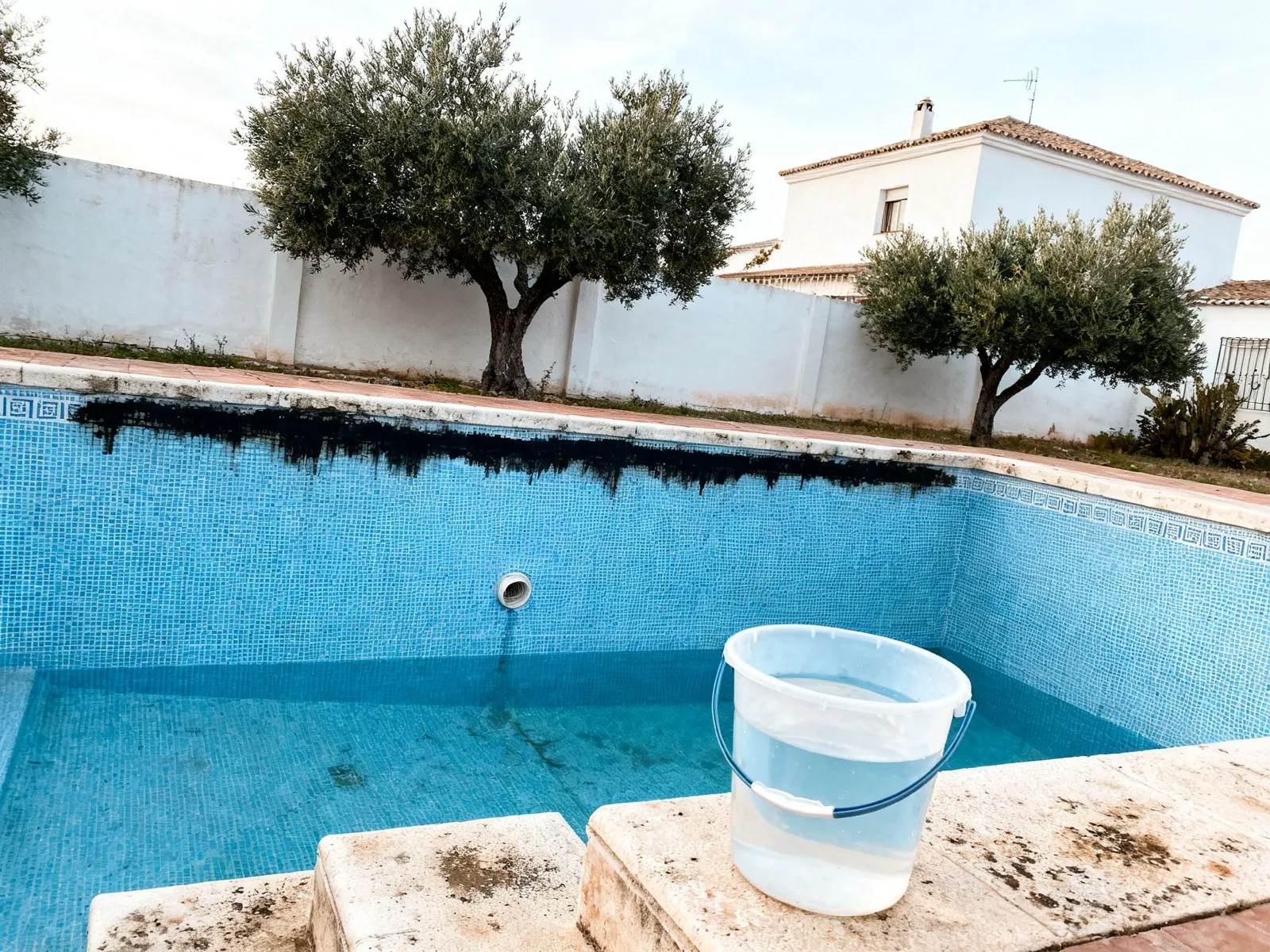 Piscina con el nivel de agua bajo y un cubo en la escalera para la prueba de pérdida de agua